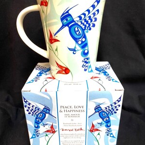 May include: A white ceramic mug with a blue and white hummingbird design and red flowers. The mug is in a box with the words "Peace, Love & Happiness" and "Paix, Amour et Bonheur" on it. The box also has the artist's name, Francis Dick, and a quote about the hummingbird.