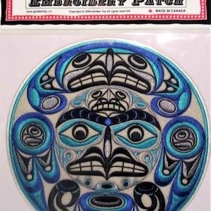 Peut inclure: Un écusson rond blanc brodé avec un motif bleu, argent et noir. Le motif représente un visage stylisé avec des yeux, un nez et une bouche. Le visage est entouré d'un motif circulaire de fleurs stylisées. L'écusson est étiqueté "Golden Top Embroidery Patch" et "Made in Canada".