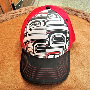 May include: A red and black baseball cap with a white and black patterned design. The pattern features stylized figures and geometric shapes.