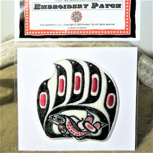May include: Embroidered patch depicting a stylised black and white bear paw with red accents, holding a salmon with green and red details. The patch is on a white background and features the text "EMBROIDERY PATCH" at the top.