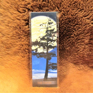 May include: A bookmark featuring a silhouette of a tree against a blue sky with a full moon. The moon is yellow and the tree is black. The bookmark has the text "Andy Everson" at the bottom.
