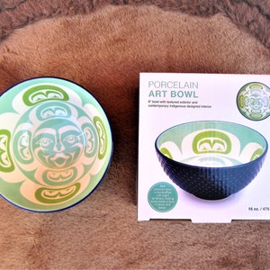 Peut inclure: Un bol en porcelaine de 15 cm de diamètre avec un extérieur texturé et un design indigène contemporain. Le bol est vert et blanc avec un motif de visage stylisé. Le bol a une capacité de 475 ml.