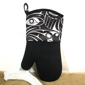Puede incluir: Manopla de horno negra con un diseño blanco y negro de inspiración nativa americana. La parte superior presenta un patrón detallado, mientras que el área de la palma tiene una superficie texturizada. Se adjunta un lazo para colgar.