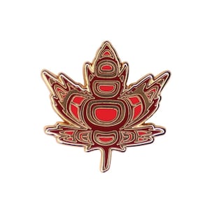 May include: A gold and red enamel pin in the shape of a stylised maple leaf. The leaf is outlined in gold and filled with red and gold geometric patterns.