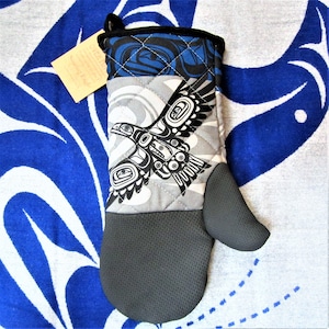 May include: A gray and black oven mitt with a quilted design featuring a stylized black and white eagle with a blue and black background. The mitt has a black heat-resistant layer on the back.