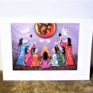 May include: A colorful painting of seven women sitting in a circle around a fire. They are all wearing different colored clothing and have long dark hair. The women are looking up at a large red moon with stars in the sky. There are white butterflies flying around the moon.