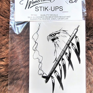 May include: Black and white decal of an eagle holding a pipe with feathers. The decal is packaged in a clear plastic bag with a white card that reads "Woodland STIK-UPS QUALITY DECALS SILK-SCREENED ON WEATHER RESISTANT CLEAR POLYESTER, VINYL OR MYLAR".