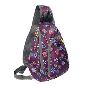 Peut inclure: Sac à bandoulière violet avec un motif floral. Le sac présente un fond violet foncé avec un motif répété de fleurs rouges, bleues et blanches. Il a une sangle grise et des fermetures éclair jaunes.