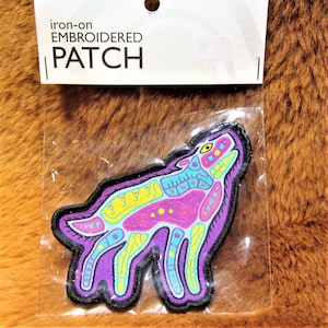 Può includere: Toppa ricamata da stirare con un design di lupo colorato. Il lupo è viola, blu, giallo e rosa con contorni neri. La toppa è confezionata in un sacchetto di plastica trasparente con un'etichetta bianca che recita "toppa ricamata da stirare".