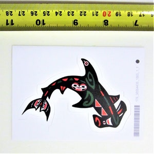 May include: A black and green hammerhead shark sticker with red and white accents. The shark is stylized in a Native American design.