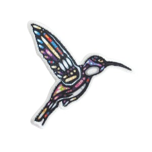May include: Hummingbird patch with a colourful stained-glass design. The patch has a black outline and a white border. The wings are filled with various colours, including blue, purple, and yellow. The hummingbird's body is mainly black with pink and purple accents.