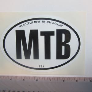 Peut inclure: Autocollant ovale blanc avec du texte noir qui dit "THE ULTIMATE MOUNTAIN BIKE MAGAZINE" et "MTB" avec "USA" en dessous du texte.