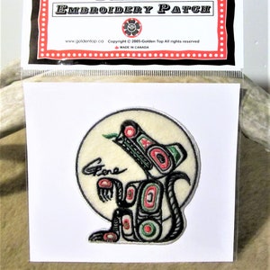 Könnte beinhalten: Ein gestickter Aufnäher mit einem schwarzen und grünen Wolf mit roten und weißen Akzenten. Der Wolf heult zum Mond, der als weißer Kreis dargestellt ist. Der Aufnäher ist mit "Stone" in schwarzer Kursivschrift signiert.