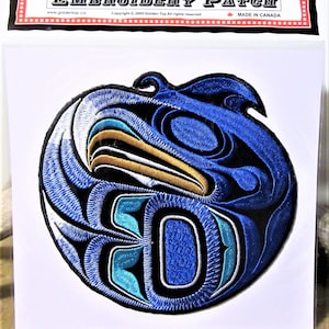Può includere: Toppa ricamata con un designo stilizzato di testa di uccello in blu, bianco e oro. La toppa è circolare e ha un contorno nero. Il testo "EMBROIDERY PATCH" è stampato nella parte superiore dell'immagine.