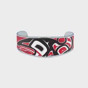 May include: A silver cuff bracelet with a red, black, and white design. The bracelet features a Native American-inspired pattern. The design is a stylized representation of an animal.