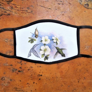 May include: A black face mask with a white background featuring a watercolour illustration of three hummingbirds and white flowers.