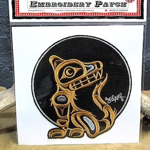 Può includere: Toppa ricamata con un disegno stilizzato di orso dorato e argentato su sfondo nero circolare. La toppa è su un supporto bianco con la scritta "EMBROIDERY PATCH" in alto. È visibile anche la scritta "MADE IN CANADA".