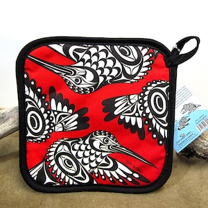 May include: Red pot holder with a black border and a design of three black and white hummingbirds. The design is in a Northwest Coast style. The text "Jane Pritchard" is in the bottom right corner.