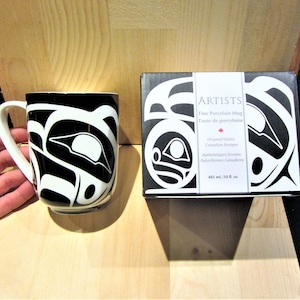 May include: A black and white porcelain mug with a Native American design. The mug is in a box with the words "ARTISTS Fine Porcelain Mug Tasse de porcelaine Original Native Canadian Designs Authentiques Dessins Autochtones Canadiens 485 ml/10 fl. oz" printed on it.