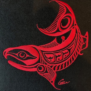 May include: Red embroidered salmon design on a black fabric background. The salmon is stylised with geometric patterns and a crescent moon shape. The artist's signature is visible in the bottom right corner.