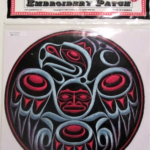 May include: Circular embroidered patch with a Native American-inspired design in black, red, and pale blue. The patch has the text "EMBROIDERY PATCH" and "MADE IN CANADA". The design features a central face and bird-like motifs.