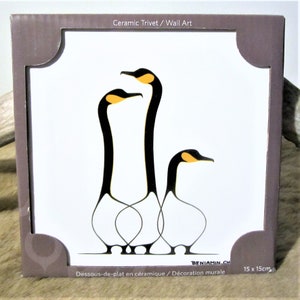 Könnte beinhalten: Keramik-Untersetzer mit einem stilisierten schwarzen und gelben Design von drei Gänsen. Der Untersetzer ist 15 cm x 15 cm groß und trägt die Aufschrift "Ceramic Trivet / Wall Art" und "Dessous-de-plat en céramique / Décoration murale".