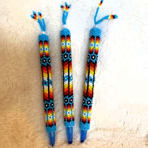 Peut inclure: Trois stylos perlés avec des perles bleues, blanches, orange, jaunes et noires en motif géométrique.