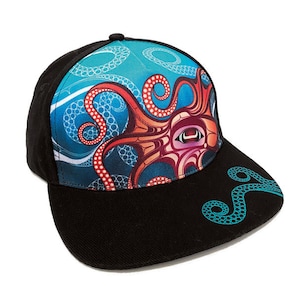 May include: A black and blue baseball cap featuring a colourful octopus design. The octopus is red, orange and white with a blue eye. The cap has a curved brim and a black strap.