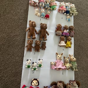 May include: A collection of flocked miniature animal figurines arranged in groups on white paper, labelled with numbers one through eight. The set includes various rabbits, bears, cats, and squirrels wearing fabric clothing in diverse colours and patterns.