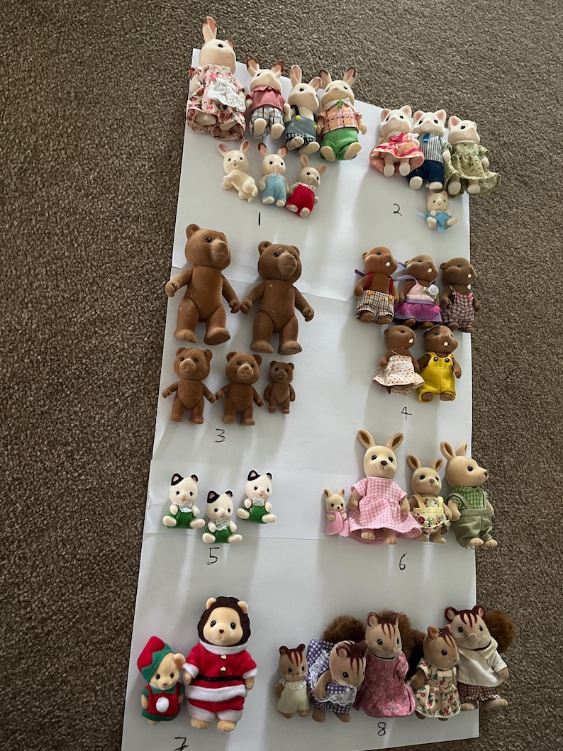 May include: A collection of flocked miniature animal figurines arranged in groups on white paper, labelled with numbers one through eight. The set includes various rabbits, bears, cats, and squirrels wearing fabric clothing in diverse colours and patterns.