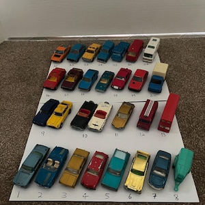 May include: A selection of miniature toy cars in diverse colours, such as red, blue, yellow, and green, displayed on a white surface. The toy cars are numbered from 1 to 27, showcasing different models and styles.