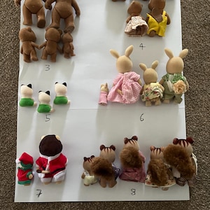 May include: A collection of flocked animal figurines arranged in groups on white paper labelled with numbers 3 through 8. The set includes various bears, rabbits, cats, and squirrels wearing fabric clothing, viewed from the back to show their outfits.