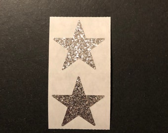 May include: Two silver glitter star stickers on a white sheet of paper.