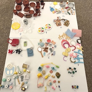 May include: A collection of miniature dollhouse accessories, including cookware, plates, purses, and beauty items, arranged on a white surface. The items are in various colors, such as brown, red, blue, and yellow.