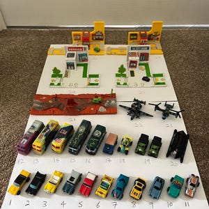 Pode incluir: Uma coleção de carros, caminhões e aviões de brinquedo, incluindo um posto de gasolina amarelo, uma ponte vermelha e uma variedade de veículos em miniatura. Os carros são de várias cores e designs, alguns com listras de corrida e logotipos.