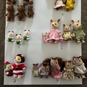 May include: A collection of flocked animal figurines arranged in groups on a white surface, labelled with numbers 3 through 8. The figures include bears, rabbits, and squirrels wearing various fabric outfits like dresses, overalls, and holiday-themed clothing.