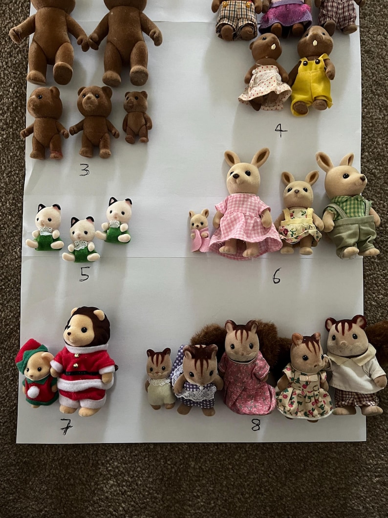 May include: A collection of flocked animal figurines arranged in groups on a white surface, labelled with numbers 3 through 8. The figures include bears, rabbits, and squirrels wearing various fabric outfits like dresses, overalls, and holiday-themed clothing.