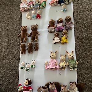 May include: A collection of flocked animal figurines arranged in groups on a white sheet, labelled with numbers 1 through 9. The set includes various rabbits, bears, squirrels, and other creatures wearing miniature fabric clothing in diverse colours.