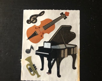 May include: A sheet of stickers featuring musical instruments, including a black grand piano, a brown violin, a gold trumpet, and a treble clef.