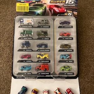 Può includere: Un set di giocattoli Micro Machines Super 15 Collection contenente quindici veicoli in miniatura. Dieci auto e camion sono sigillati in una confezione blister di plastica con etichette, mentre cinque auto giocattolo sfuse sono posizionate sotto.