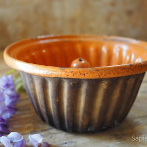 May include: Orange and brown ceramic bundt cake pan with a fluted design. The pan has a central tube for a cake to be baked around.
