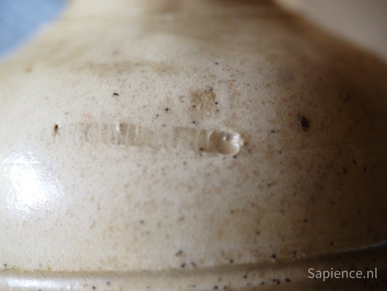 May include: Close-up of a cream-colored ceramic crock with a brown glaze and a faint inscription that reads "United States".