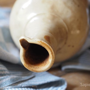 May include: Close-up of the opening of a vintage ceramic pitcher with a light brown glaze. The inside of the pitcher is stained a dark brown.