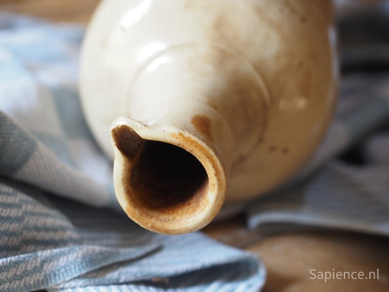 May include: Close-up of the opening of a vintage ceramic pitcher with a light brown glaze. The inside of the pitcher is stained a dark brown.