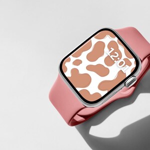 May include: A pink Apple Watch with a white and brown cow print watch face. The time is 12:01.