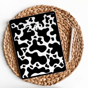 May include: A black and white cow print iPad screen protector with a digital clock displaying 2:49. The iPad is on a woven straw placemat.