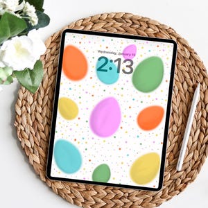 Puede incluir: Un iPad muestra un fondo de pantalla con temática de huevos de Pascua. La pantalla muestra huevos de colores pastel, incluyendo naranja, rosa, verde, amarillo y azul, sobre un fondo blanco con pequeños puntos. La hora es 14:13, miércoles 15 de enero.