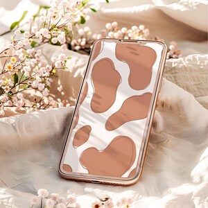 May include: A gold smartphone with a white and brown abstract pattern on the screen. The phone is lying on a white fabric surface with white flowers.