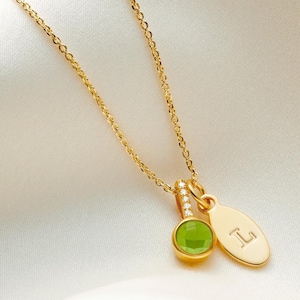 May include: Gold necklace with a green gemstone pendant and a small oval charm with the letter "L" engraved on it.