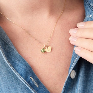 Pode incluir: Um colar de corrente de ouro com um pingente de pedra preciosa verde e um amuleto em forma de coração gravado com a letra "K".